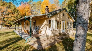 Une cabane en bois avec une véranda, une cheminée et une terrasse.
