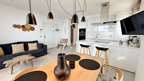Una cocina moderna con un televisor de pantalla plana, un comedor con una mesa y sillas de madera, y una sala de estar con sofá y decoración mural.