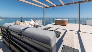 Eine Dachterrasse mit einer Couch, einem Hocker, einem Whirlpool und freiem Blick auf das Meer.