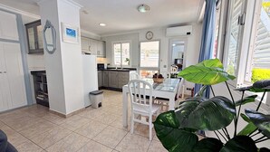 Una cocina con armarios blancos, una mesa de comedor con sillas y una planta verde grande.