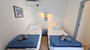 Habitación doble con dos camas, una mesita de noche, aire acondicionado de pared y un cuadro enmarcado.