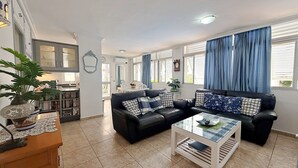 Una sala de estar con un sofá de cuero negro, una mesa de centro de vidrio y una estantería.