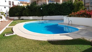 Una piscina con una zona verde circundante y un edificio blanco al fondo.