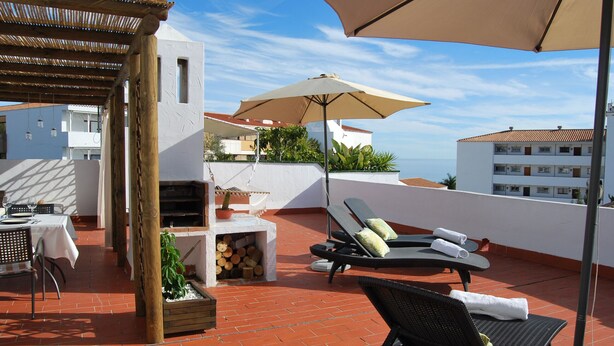Una terraza en la azotea con sillones de descanso, una mesa y una pérgola.