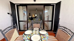 Um pátio aberto com uma mesa de jantar posta para dois, uma cadeira de vime e vista para uma sala de estar com um sofá e escada.