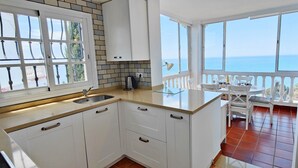 Una cocina con armarios blancos, un lavamanos y vistas al mar a través de ventanas amplias.