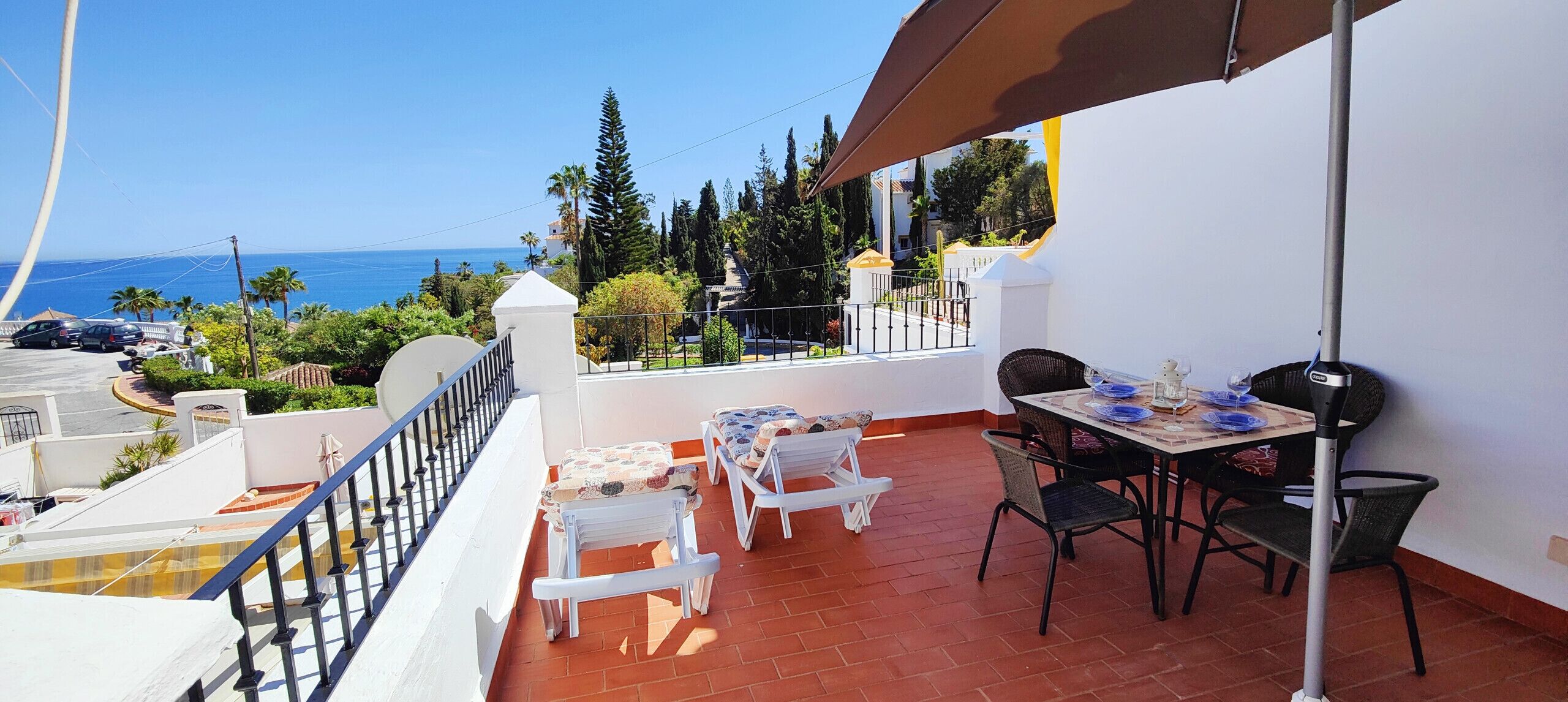 Un balcon avec une table et des chaises, donnant sur une zone côtière bordée de palmiers et offrant une vue sur la mer.