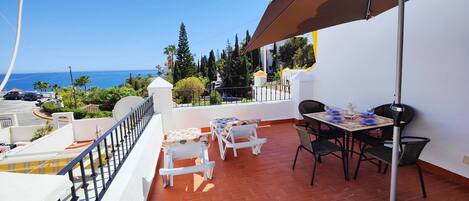 Un balcon avec une table et des chaises, donnant sur une zone côtière bordée de palmiers et offrant une vue sur la mer.