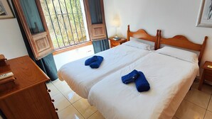 A double bed with white linens and two blue towels, wooden headboard, bedside tables with lamps, and a window with bars. - AP346 TORROX BEACH (Torrox Costa)