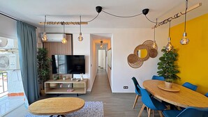 Una sala de estar moderna con televisor, mesa de comedor, sillas y lámparas colgantes.