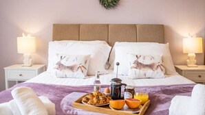A neatly made bed with two pillows featuring a rabbit design, a tray with croissants, a bottle of jam, and a glass of orange juice.