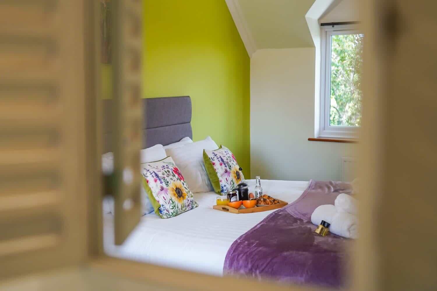 A bedroom with a bed, pillows, a tray with breakfast items, and a window.