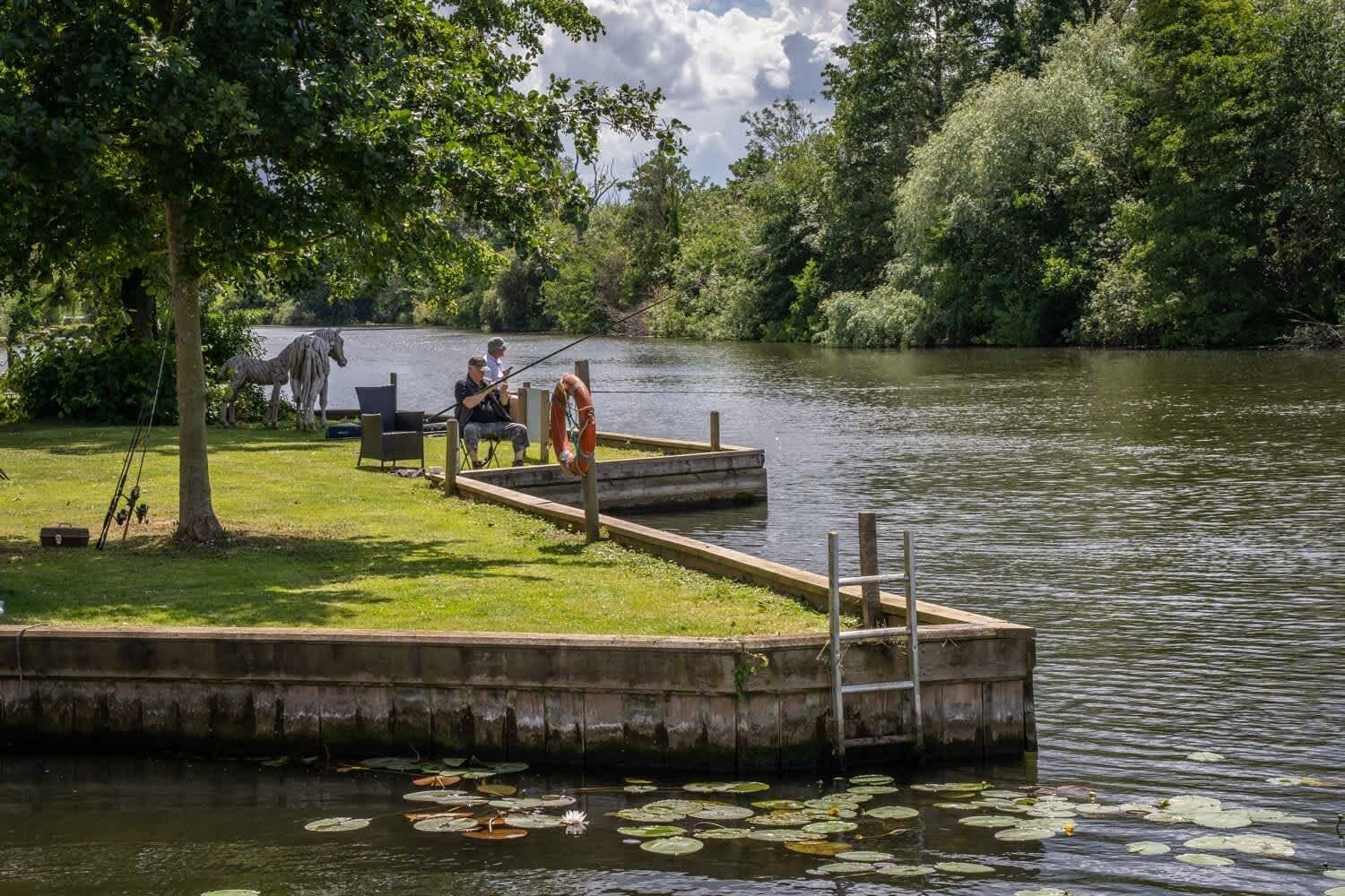 A dock extending into a lake with lily pads, surrounded by lush greenery and trees.