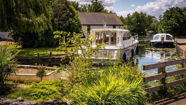 A canal with boats docked, a wooden bridge, and lush greenery.