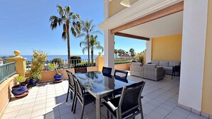 A terrace with a glass table and chairs, a sofa, potted plants, and a view of the sea. - AP191 SEÑORIO DE CAPISTRANO (Nerja)