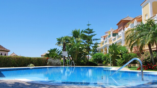 A swimming pool surrounded by palm trees and buildings with tiled roofs. - AP191 SEÑORIO DE CAPISTRANO (Nerja)