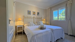 Een slaapkamer met twee bedden, nachtkastjes met lampen, een raam met gordijnen en drie ingelijste foto's aan de muur.