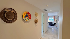 Een gang met decoratieve hoeden aan de muur, die leidt naar een kamer met uitzicht op zee.