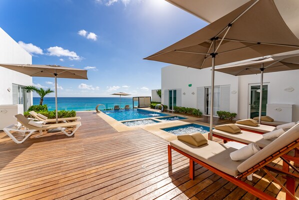 A wooden deck with sun loungers and umbrellas, a pool, and a view of the ocean. - Suite Deluxe, Cerca de las Olas, Vista al mar (Cancún)
