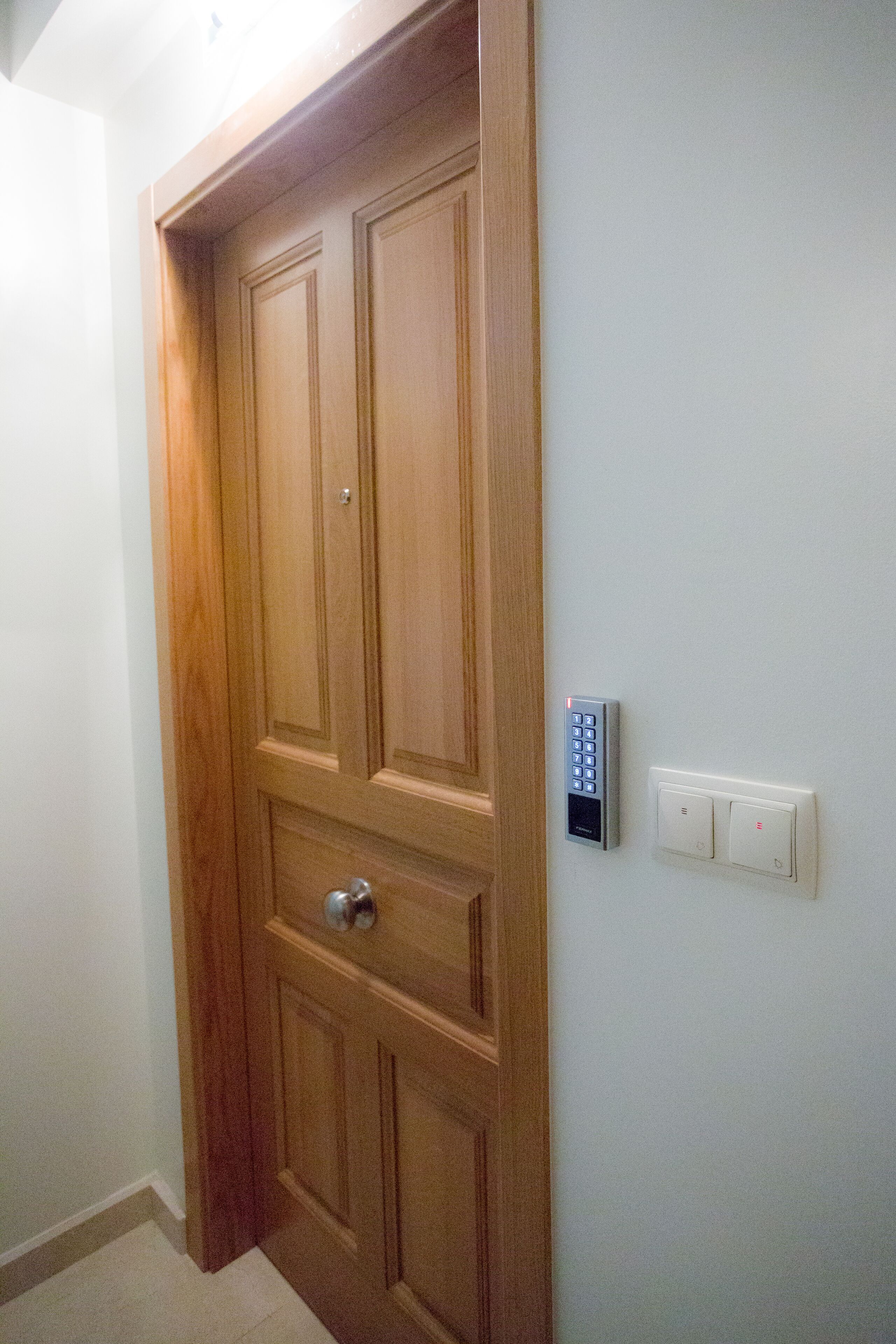 A wooden door with a keypad lock and a light switch on the wall.