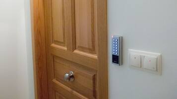 A wooden door with a keypad lock and a light switch on the wall.