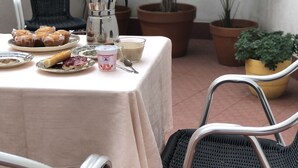 Ein Tisch gedeckt mit Gebäck, einer Kaffeekanne und einem Getränk, umgeben von Korbstühlen und Topfpflanzen.