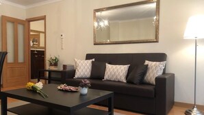 Ein Wohnzimmer mit einem dunklen Sofa, einem Couchtisch, einer Lampe und einem großen Spiegel an der Wand.