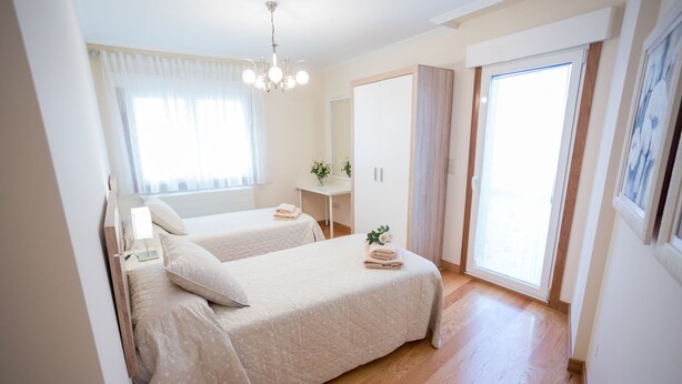 Ein Schlafzimmer mit zwei Betten, einem Nachttisch, einem Spiegel, einem Kleiderschrank und einem Fenster mit Vorhängen.