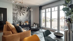 En moderne stue med sofa, lænestole, sofabord og et stort vindue med udsigt over byen.