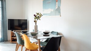 Et spiseområde med et glasbord, farverige stole, en vase med blomster og et billede på væggen.