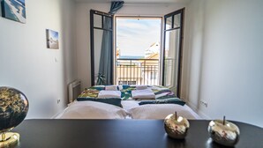 Et hotelværelse med en seng, et skrivebord og havudsigt gennem åbne vinduer.