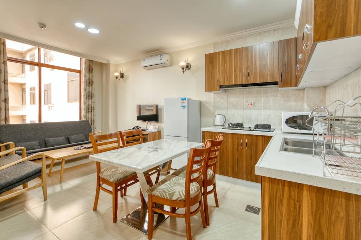 A modern kitchen with wooden cabinets, a dining table with chairs, a built-in oven, and a large window.