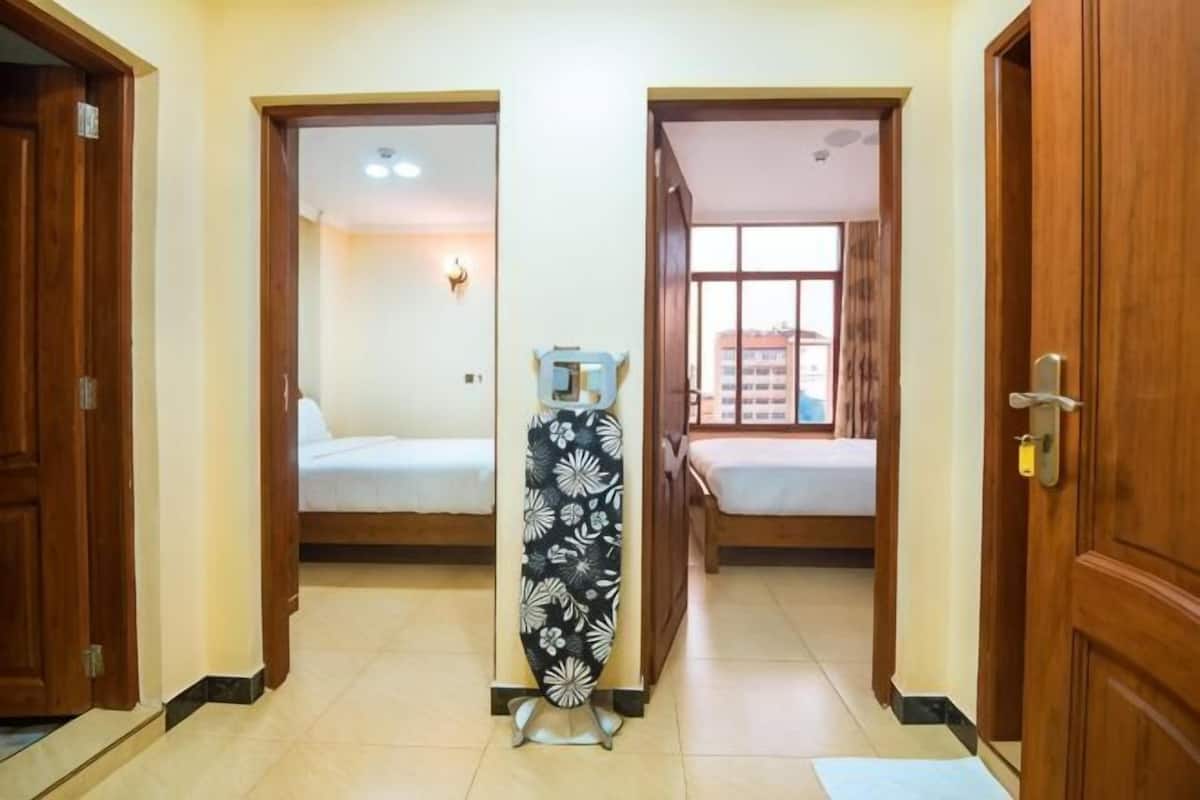 A hallway with two bedrooms, a wooden door on the right, and a window on the left.