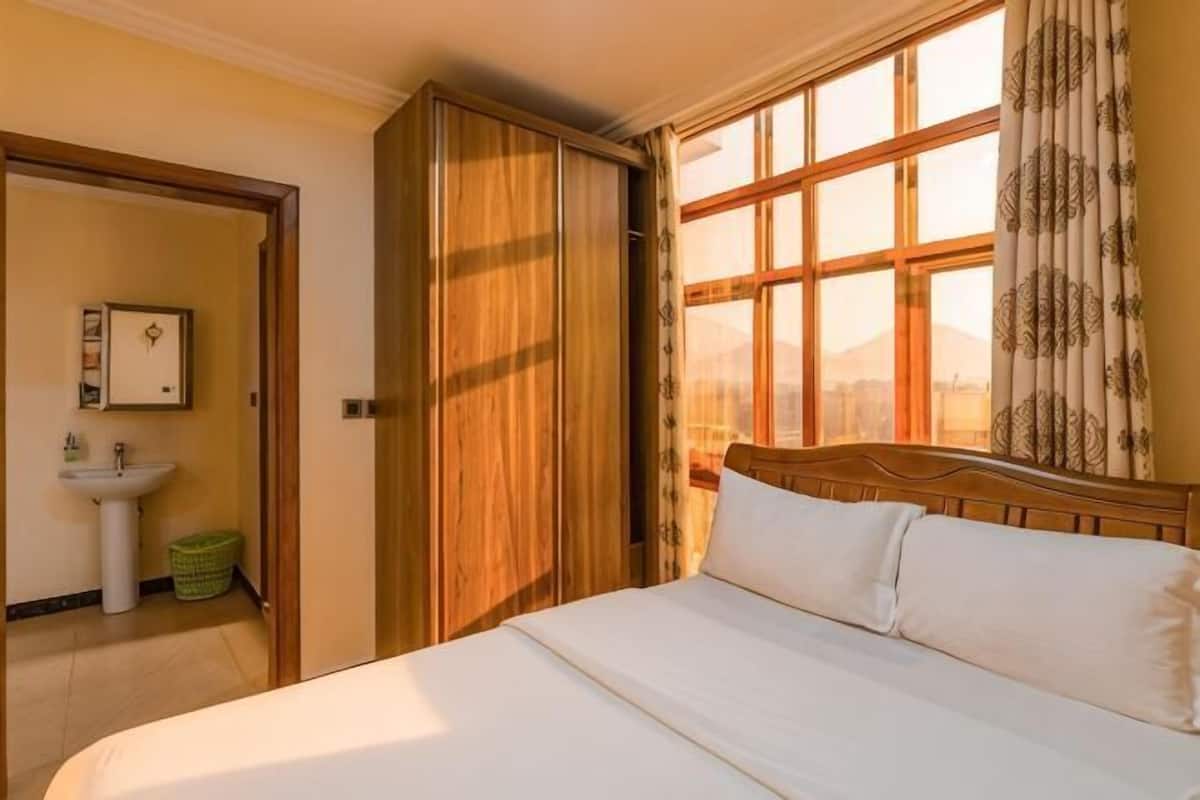 A hotel room with a bed, a window with curtains, a wardrobe, and a sink.