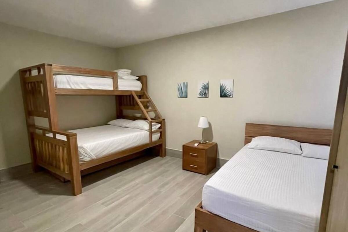 A room with a bunk bed, a single bed, a nightstand, and a wall with three small plant pictures.