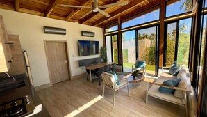 A spacious living area with a wooden ceiling, large windows, a dining table, and a sofa.