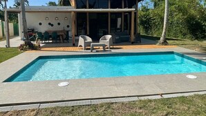 A swimming pool with lounge chairs, a covered patio area, and palm trees in the background.