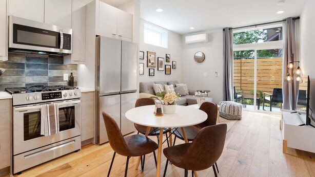 Una cocina moderna con electrodomésticos de acero inoxidable, un comedor con una mesa redonda y sillas, y un amplio ventanal con vistas al exterior.