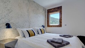 A bedroom with a large bed, two bedside lamps, a window with a view of trees, and a textured wall. - Carlina 203 Beautiful ski in ski out 2 bed + cabin  in the heart of the village (MORZINE)