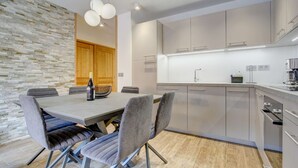 A modern kitchen with grey cabinets, a wooden door, and a dining area with a table and chairs. - Carlina 203 Beautiful ski in ski out 2 bed + cabin  in the heart of the village (MORZINE)