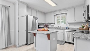 A modern kitchen with white cabinetry, a granite countertop island, stainless steel appliances, and a window with blinds. - The best of Huntsville: Mountain view & Attraction. (Huntsville)
