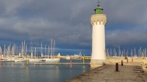 Un phare doté d’une base en pierre et d’une partie supérieure verte, entouré d’une marina où sont amarrés de nombreux voiliers.
