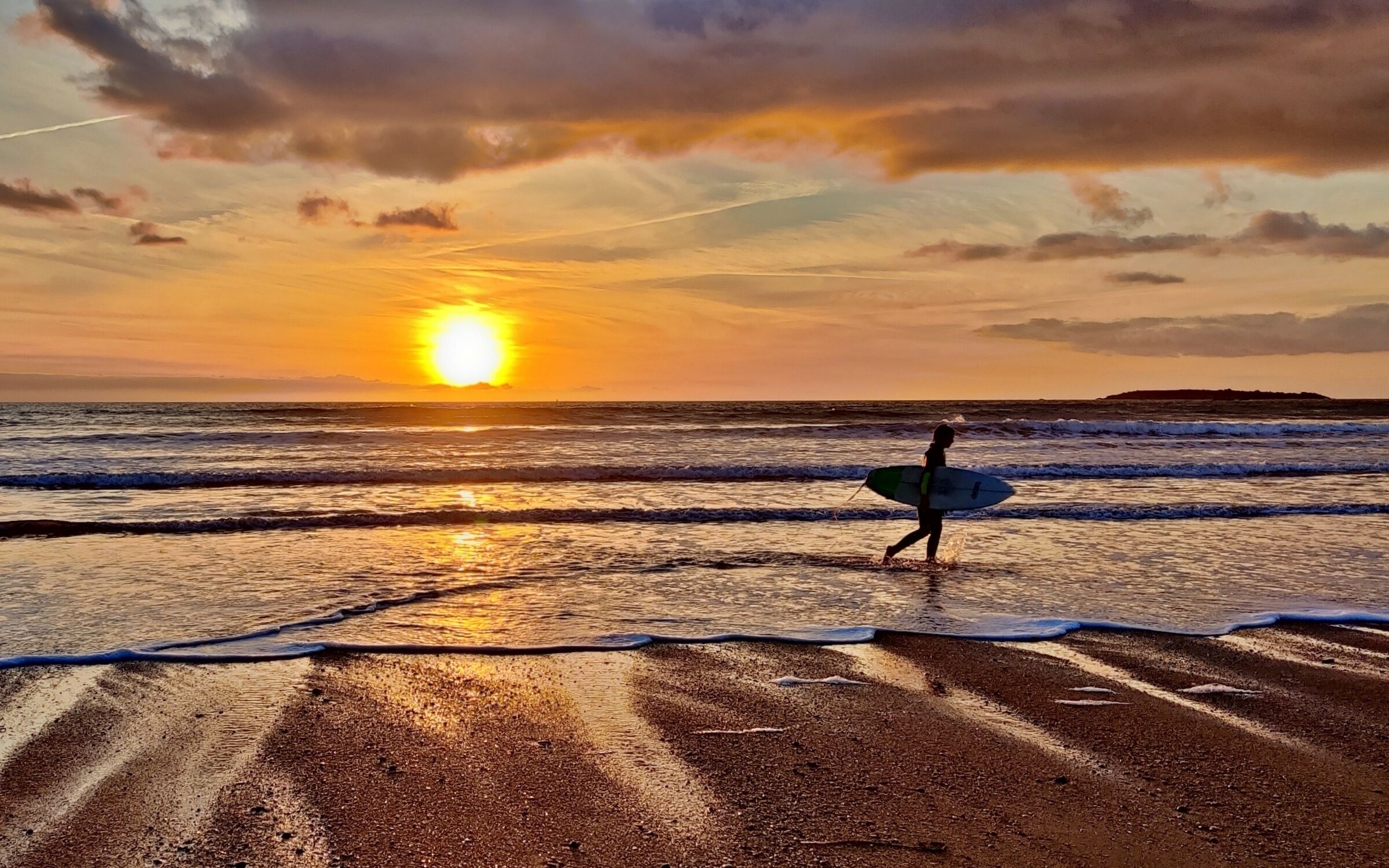 Ein Sonnenuntergang über einem Strand, eine Person trägt einen Surfbrett.