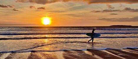 Ein Sonnenuntergang über einem Strand, eine Person trägt einen Surfbrett.