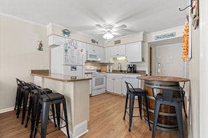 A kitchen with white cabinets, a microwave, a stove, and a bar area with stools.