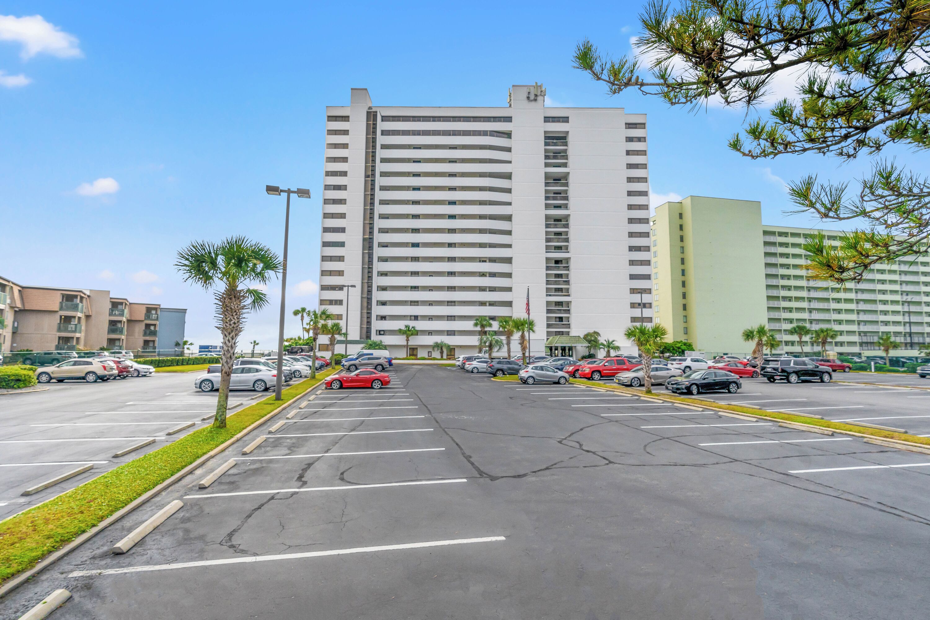 A parking lot with multiple cars, a tall building with a flat facade, and palm trees.