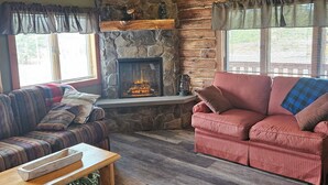 Un salon chaleureux avec une cheminée en pierre, des poutres en bois et deux canapés.