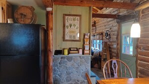 L’intérieur d’un chalet rustique, avec un mur en pierre, des poutres en bois, un réfrigérateur noir, une table à manger en bois et un tableau illustré présentant différentes herbes.