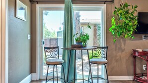 A room with a sliding glass door leading to a patio, a small round table with two chairs, a hanging plant, and a TV mounted on the wall. - Red Rocks, HOT TUB, W. Sedona, Walk to trls, 1 bd! (Sedona)