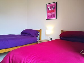 Een slaapkamer met twee bedden, elk met een anderkleurige spreideken, een nachtkastje met een lamp en een poster aan de muur.